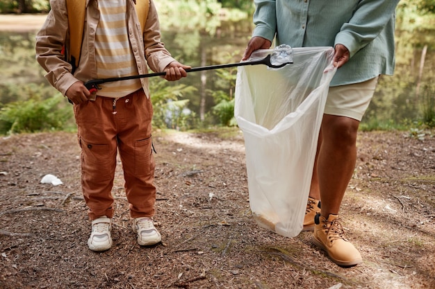 Niño recortado ayudando a limpiar la naturaleza y recogiendo botellas de plástico al aire libre