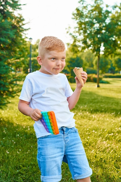 El niño redhear sostiene una burbuja, un juguete antiestrés sensorial flexible, hazlo estallar o simplemente, un hoyuelo y un helado