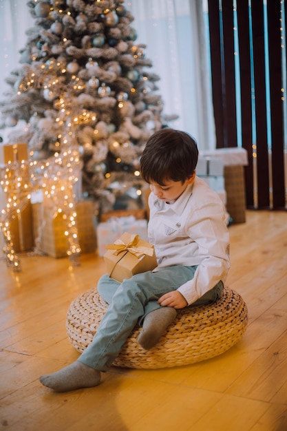 Un niño con un regalo de año nuevo bajo el estilo de vida del árbol. Año Nuevo y Navidad. Decoración festiva.