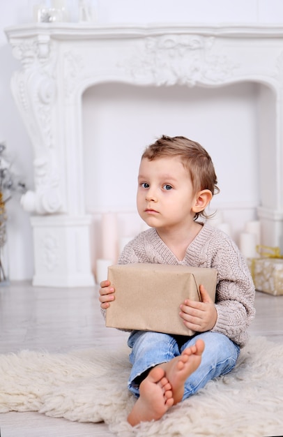 Niño con regalo cerca de la chimenea.