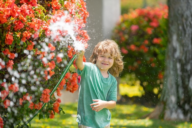 Niño regando flores y plantas en el jardín niño con manguera de agua en el patio trasero niños jardinería niños summ