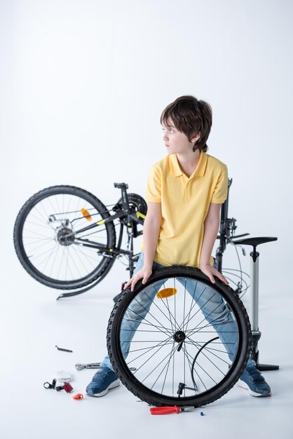 Foto niño reparando un neumático de bicicleta en un estudio en blanco