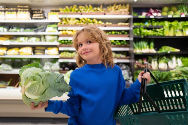 Niño con repollo niño eligiendo frutas y verduras durante las compras en el supermercado de verduras