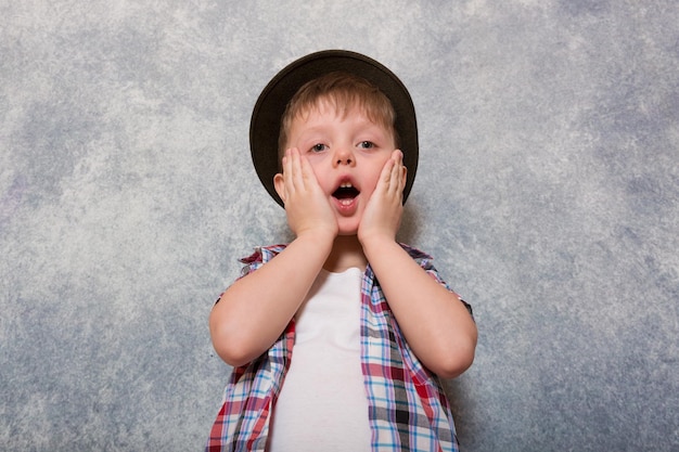 Un niño ridículo vestido con una camisa a cuadros roja y un sombrero hace caras diferentes