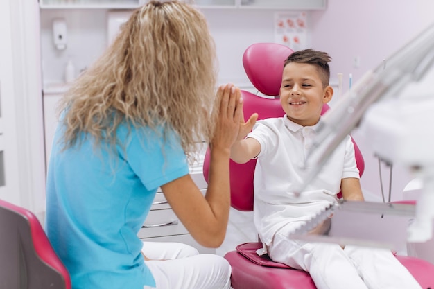 El niño se ríe y hace una mano de respeto con una mujer dentista después de una visita y examen en odontología