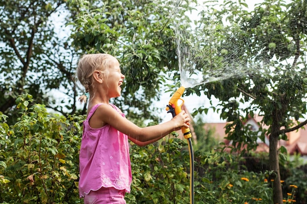 Niño riega el jardín con una manguera de jardín Chica alegre juega con agua