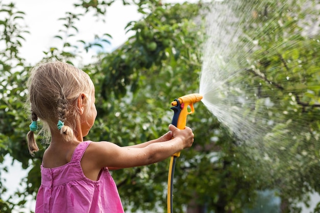 Niño riega el jardín con una manguera de jardín Pulverización de agua en los árboles verdes