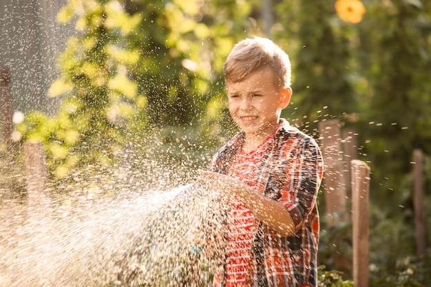 El niño riega las plantas haciendo grandes salpicaduras de agua