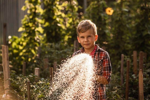 El niño riega las plantas haciendo grandes salpicaduras de agua