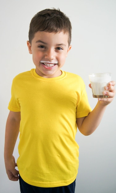 Niño riendo en camiseta amarilla con bigote de kéfir o leche y vaso en la mano