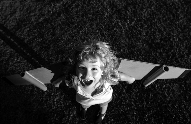 Niño riendo jugando con alas de avión de juguete en un parque de verano innovación tecnológica y concepto de éxito