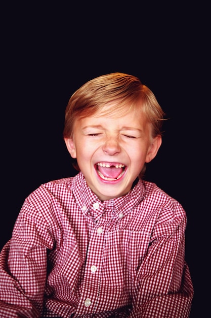 Foto niño riendo con los ojos cerrados contra un fondo negro