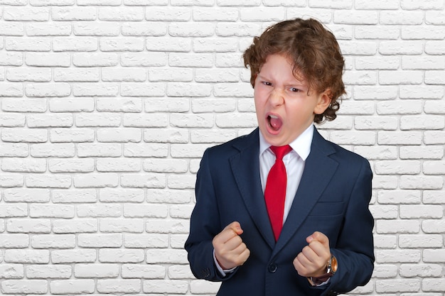 Niño rizado enojado en un traje formal