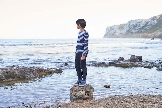 El niño se para en una roca junto al mar.