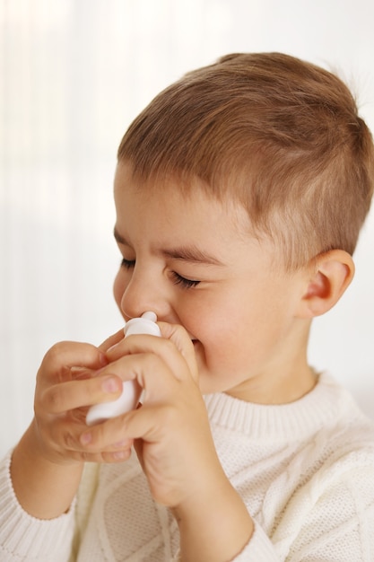 Niño rociando medicina en la nariz, gotas nasales. Niño pequeño con aerosol nasal. Secreción nasal, resfriado, gripe, enfermedad, virus. De cerca.