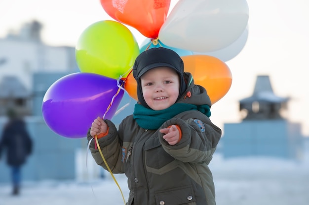 Niño en ropa de abrigo con coloridas pelotas inflables en invierno