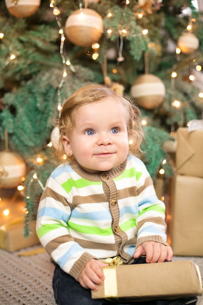 Niño con ropa de año nuevo, pasa tiempo en el árbol de Navidad