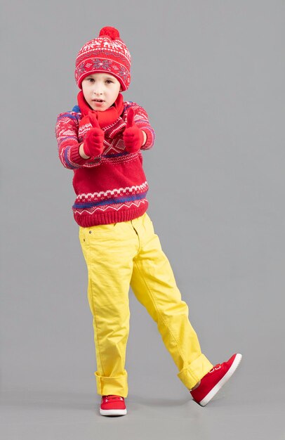 Un niño con ropa cálida y brillante Niño con bufanda de sombrero de invierno y suéter rojo y zapatillas de deporte