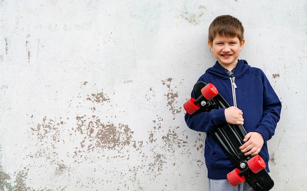 Un niño en ropa deportiva con un patín en el fondo de una pared enlucida.