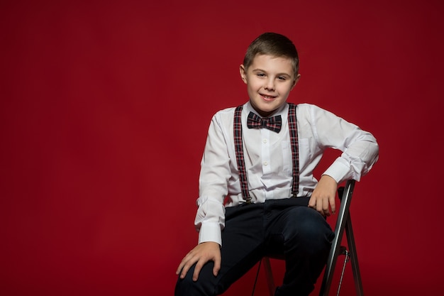 Niño con ropa elegante se sienta en una escalera de hierro contra la pared roja