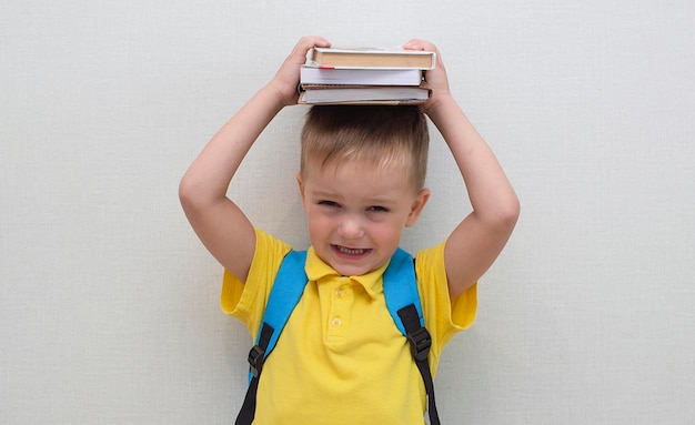 Un niño con ropa informal después de la escuela con un libro en la cabeza. Educación y lectura para un niño. De vuelta a la escuela. Curso preescolar de lectura rápida. Chico divertido tiene un libro sobre su cabeza.