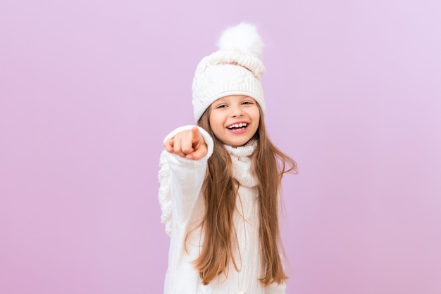Un niño con ropa de invierno señala el espacio frente a él y sonríe contra un fondo rosa aislado.