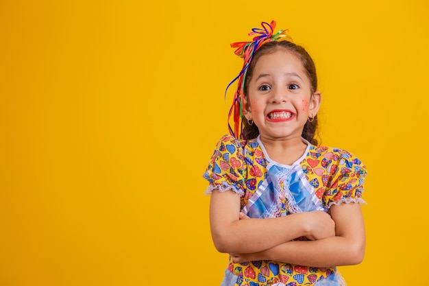 Niño con ropa típica de la famosa fiesta brasileña llamada Festa Junina en celebración de Sao Joao Hermosa niña sobre fondo amarillo Brazos cruzados