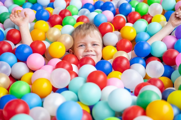 Niño rubio acostado sobre bolas de plástico multicolores en una gran piscina para niños en seco en el centro de juego