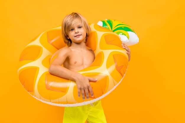 Niño rubio en bañador amarillo con círculo de natación piña en naranja