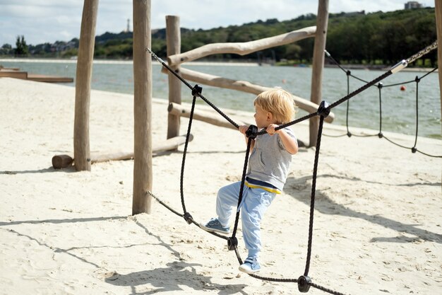 Niño rubio caucásico jugando en el parque infantil en un día soleado de otoño.