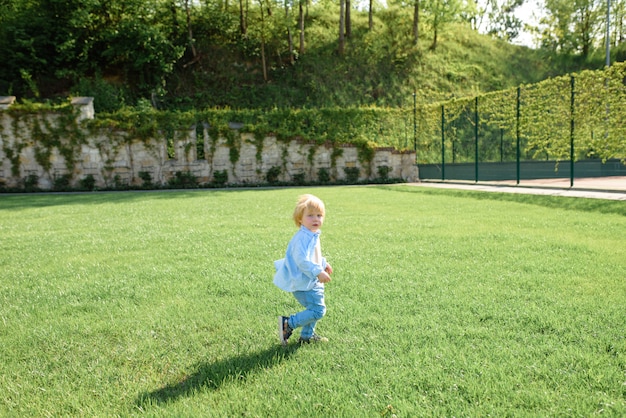Niño rubio corre sobre la hierba verde