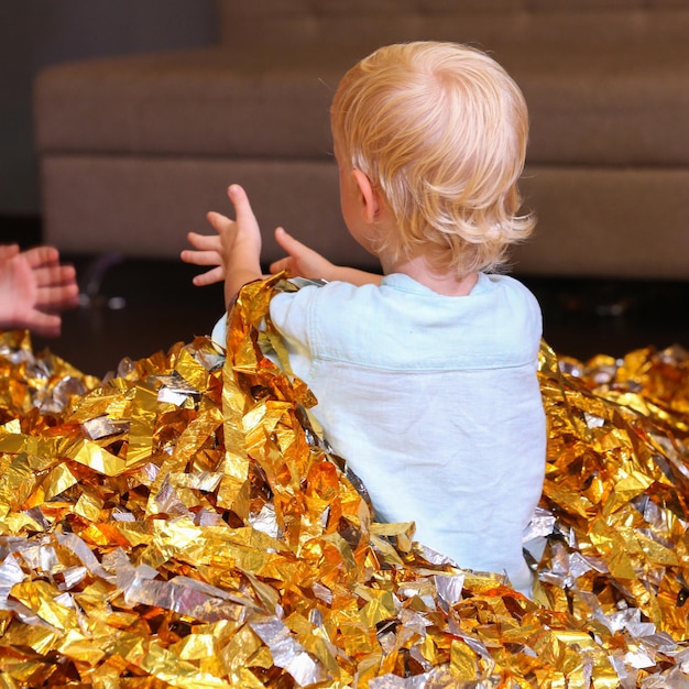 un niño rubio está sentado en una pila de papel dorado cortado