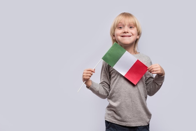 Niño rubio feliz sosteniendo la bandera de Italia sobre fondo blanco Educación en Italia