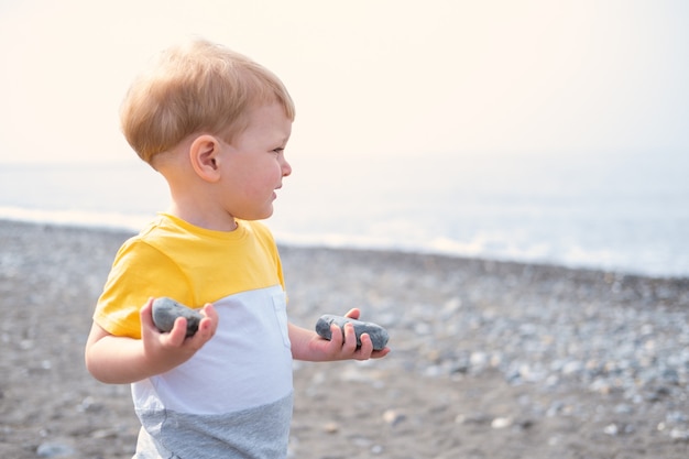 Niño rubio jugando con rocas y arena en la playa en un día soleado