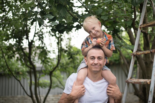 Niño rubio con una manzana en sus manos sobre los hombros de su padre.