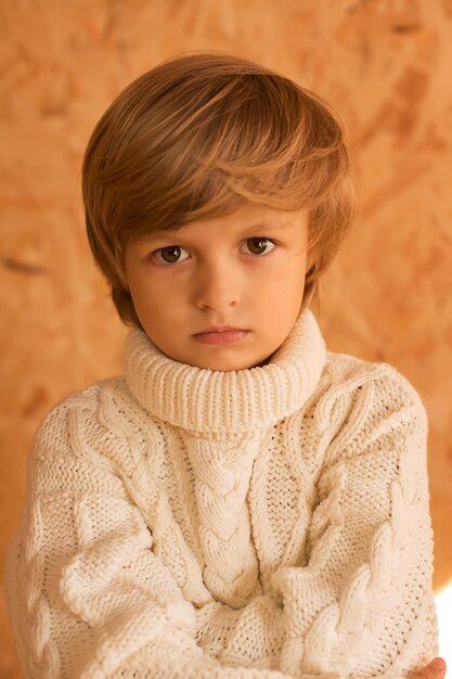 un niño rubio pensativo en un suéter de punto blanco sobre un fondo amarillo