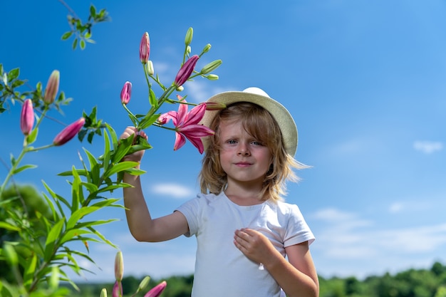 niño rubio con un sombrero blanco camina en el jardín verde y huele flores