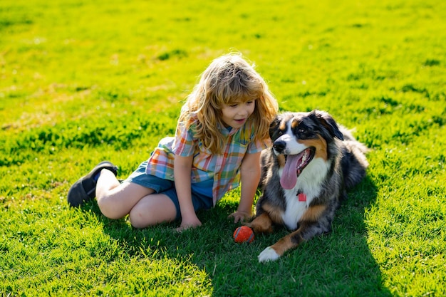 Niño rubio con su perro mascota al aire libre en el parque Niño con cachorro de mascota Un niño con un perro jugando en la naturaleza en la hierba verde