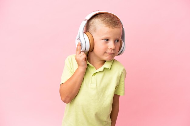 Un niño ruso aislado de fondo rosa escuchando música haciendo gestos de rock