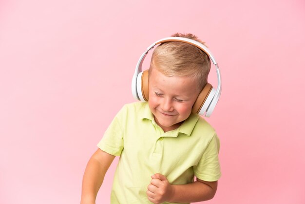 Un niño ruso aislado de fondo rosa escuchando música y con el pulgar hacia arriba