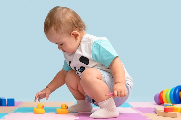 Niño en la sala de juegos agarra patitos de goma amarillos para bañarse desde el suelo