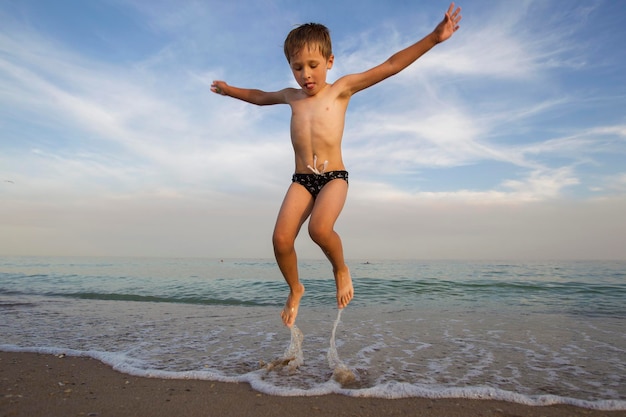 El niño salta fuera del agua El niño salta sobre el océano Vacaciones en la playa