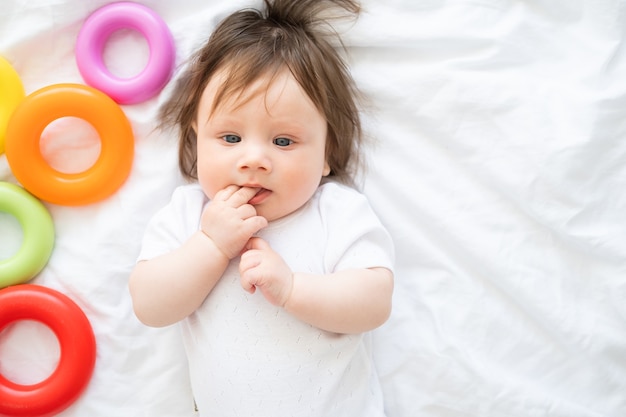 Niño sano acostado en la cama y jugar con el juguete del círculo de plástico de colores.