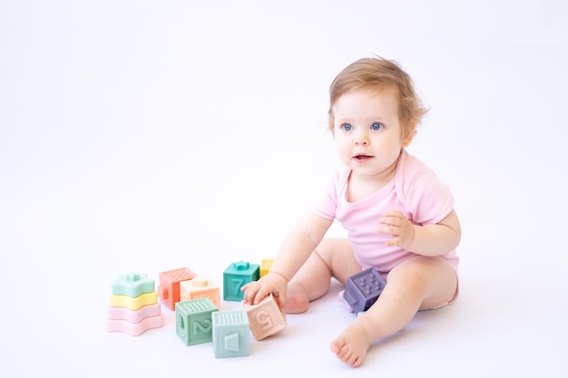 Un niño sano y lindo con un traje rosa está sentado y jugando con cubos coloridos en un fondo blanco, un lugar para el texto