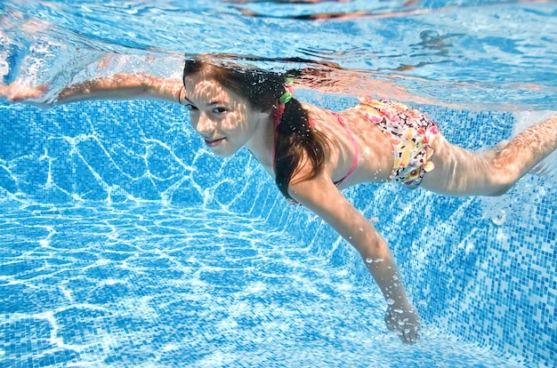 Niño sano nada bajo el agua en la piscina niña activa se sumerge y se divierte bajo el agua