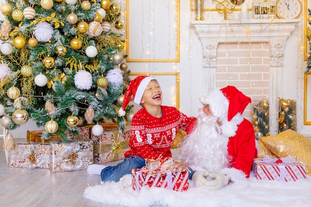 Un niño y Santa Claus se ríen cerca del árbol de Navidad, un niño feliz está hablando con Santa Claus