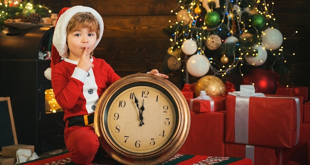 Niño santa con reloj navidad tiempo de navidad niño feliz está sentado junto al reloj grande niño está esperando f