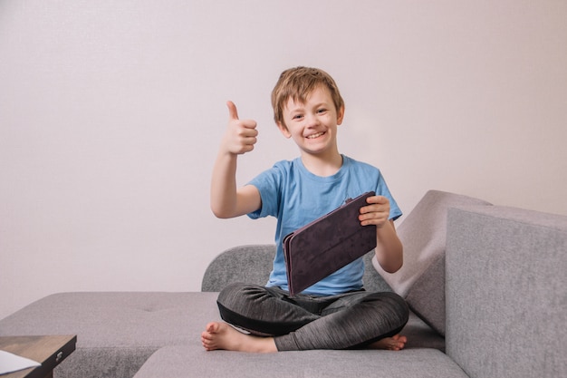 Niño satisfecho con una camiseta azul juega en el sofá con una tableta