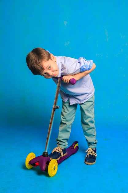 Un niño en un scooter sobre un fondo azul Un artículo sobre scooters para niños Un artículo sobre la elección de un scooter para un niño Un niño feliz Fondo azul y un niño