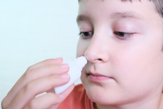 Un niño con secreción nasal sostiene un medicamento en la mano, irrigaciones en aerosol nasal para detener la rinitis alérgica y la sinusitis.